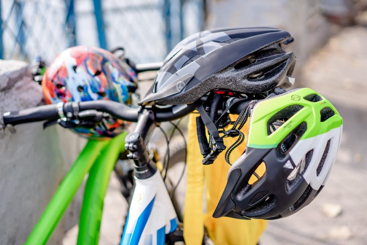 Two bike helmets hanging from bicycle handlebars